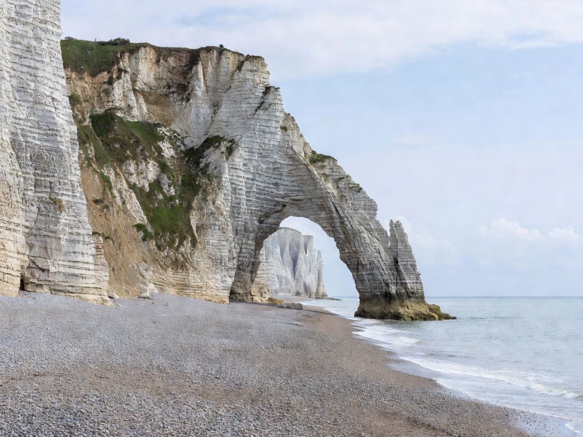 White chalk cliffs and a natural stone arch above a shingle beach on the Normandy coast